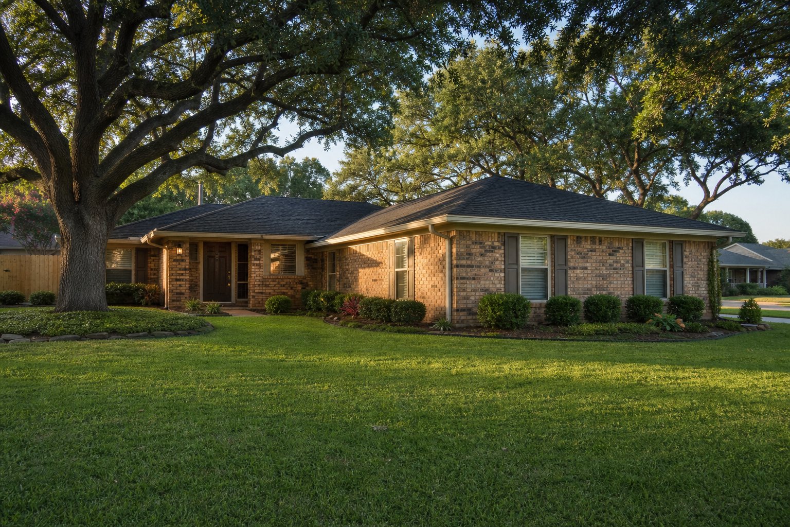 Single-story brick ranch home viewed from the front corner showing the full perimeter edge of the house and neat lawn, mature live oak shading one side
