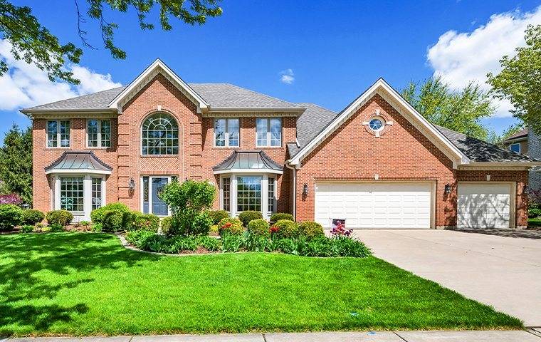 A brick home in the suburbs of Chicago with dying shrubs in Arlington.