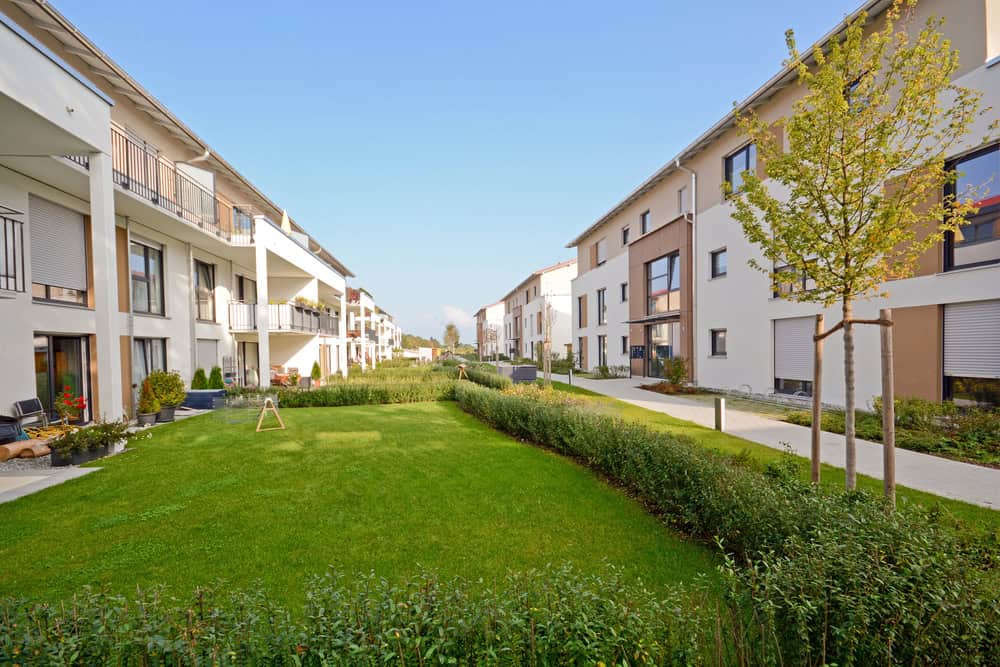 Modern apartment buildings with balconies showcase impressive apartment landscaping in a landscaped courtyard, featuring a grassy lawn and small trees under a clear blue sky.