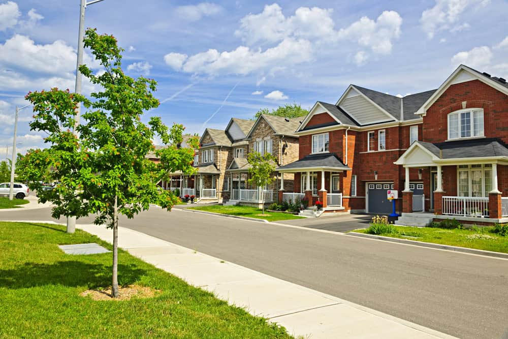 Suburban street with row of brick houses, small front yards, and a sidewalk. Managed by attentive property managers, a young tree thrives near the curb under a partly cloudy sky. Suburban street with row of brick houses, small front yards, and a sidewalk. Managed by attentive property managers, a young tree thrives near the curb under a partly cloudy sky.