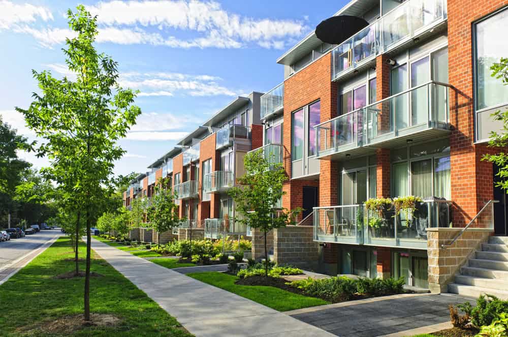 A row of modern red brick apartments with glass balconies, meticulously maintained by attentive property managers, features neatly landscaped surroundings, trees, and a sidewalk basking in the sunlight. A row of modern red brick apartments with glass balconies, meticulously maintained by attentive property managers, features neatly landscaped surroundings, trees, and a sidewalk basking in the sunlight.